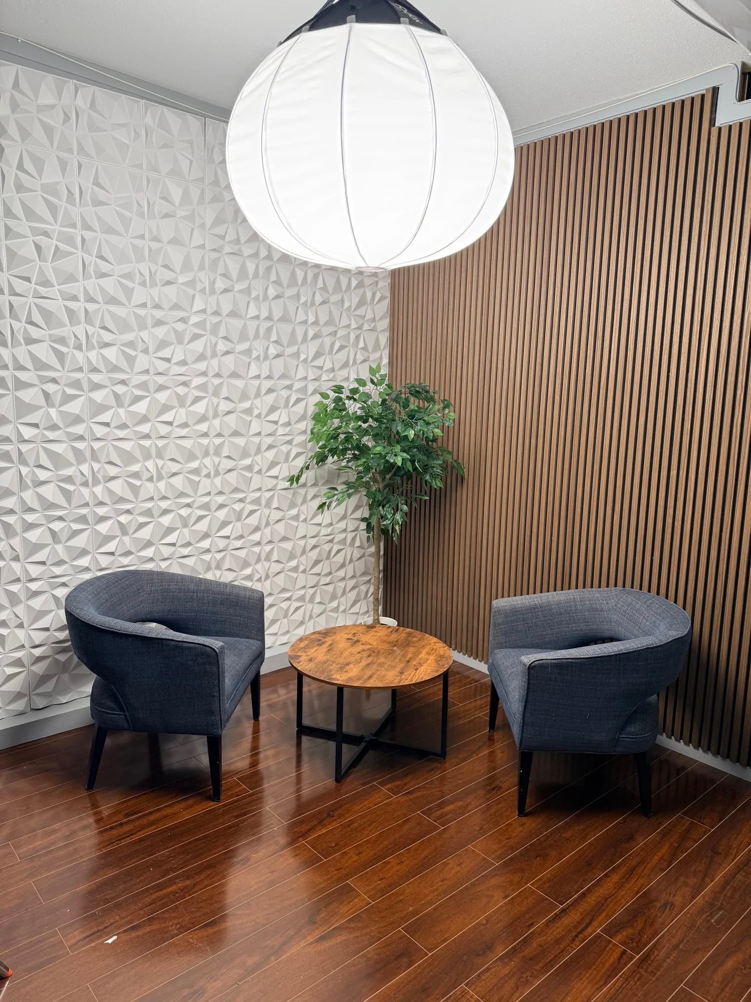 Two armchairs and a round table in front of textured and wood-slat walls